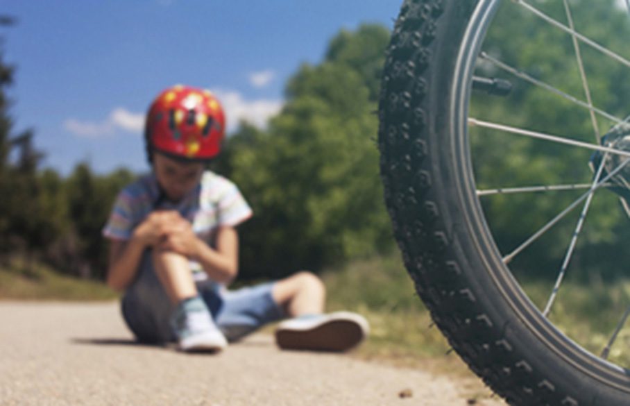 Pyörällä kaatunut lapsi istuu maassa ja hänen polvessa on haava.